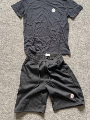 Svart t-shirt från Moncler - Snygg svart t-shirt från Moncler med klassisk logga på bröstet. T-shirten har rund hals och korta ärmar, perfekt för en clean och stilren look. Tillverkad i mjukt bomullsmaterial som känns skönt mot huden.