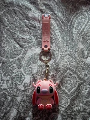 Söt rosa Stitch nyckelring - Nyckelring med en gullig rosa Stitch-figur i mjukt gummi. Figuren har stora ögon, långa öron och söta tassar. Nyckelringen har även ett rosa band med texten 'Stitch' och metallring för enkel fastsättning på väska eller nycklar. har bara använt det rosa bandet till min nyckel till mitt skolskåp💕