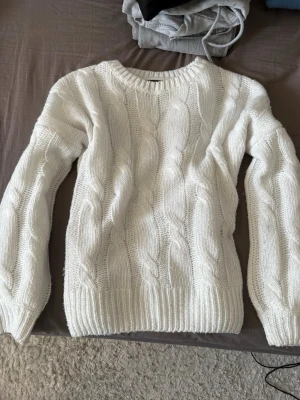 Vit kabelstickad tröja - Säljer en vit kabelstickad tröja. Tröjan har rund halsringning, långa ärmar och ribbade muddar vid ärmslut och nederkant. Perfekt för kyligare dagar och enkel att matcha med olika outfits.
