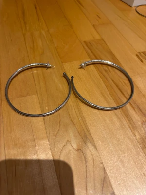 Stora silvriga hoops örhängen - Säljer ett par stora, runda hoops örhängen i silverfärgad metall. De har en enkel och stilren design som passar till många olika looks. Perfekta för dig som gillar klassiska accessoarer med lite attityd.