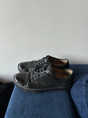 Svarta sneakers från Lanvin - Säljer ett par svarta sneakers från Lanvin med snygg kontrast mellan mocka och lackad tå. Skorna har svarta skosnören, metallfärgade öljetter och en klassisk låg profil. Perfekta för dig som gillar stilrena och exklusiva sneakers. Stl 43, passar 44. Inga defekter på själva skorna  men skösnörena e lite sådära, men ett par skosnören kostar typ 50kr så inte värsta. Kom dm för frågor!