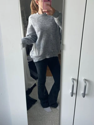 Oversized grå stickad tröja - Mysig oversized stickad tröja i ljusgrått med rund halsringning och långa ärmar. Tröjan har en avslappnad passform och ribbade muddar vid ärmslut och nederkant. Perfekt för lager på lager och chill dagar.