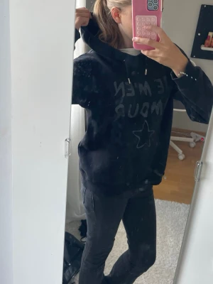 Svart hoodie med text och stjärna - Säljer en svart hoodie med huva och dragsnören. På framsidan står det 'JE NÊME AMOUR' i glittrig text och en stjärna under. Hoodien har en avslappnad passform och är perfekt för en chill look. Materialet känns mjukt och bekvämt.