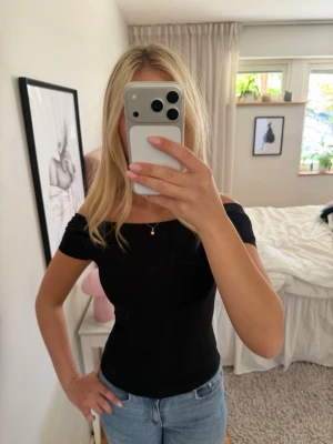 Svart öppen rygg topp  - Säljer en svart, tight offshoulder topp med korta ärmar. Toppen har en djup, rundad rygg och är tillverkad i ett stretchigt material som sitter snyggt på kroppen. Perfekt att styla med jeans eller kjol för en trendig look.