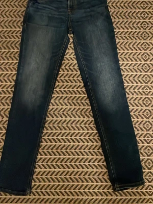 Blå jeans från Jack & Jones - Säljer ett par klassiska blå jeans från Jack & Jones med raka ben och två bakfickor. Jeansen har snygga kontrastsömmar och en läderpatch med logga bak i midjan. Perfekta till en avslappnad stil och tillverkade i mjukt denimtyg.