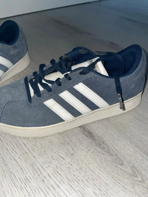 Blå Adidas sneakers i mocka - Snygga blå sneakers från Adidas i mocka med klassiska vita ränder på sidorna och vit sula. Skorna har mörkblå snören och låg profil som passar perfekt till streetwear och casual outfits.