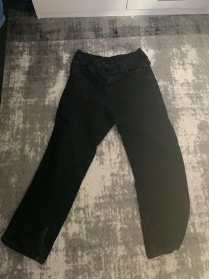 Svarta raka jeans med reflexdetalj - Säljer ett par svarta jeans med rak passform och hög midja. Jeansen har en unik reflexdetalj på ena benet baktill och klassiska fickor både fram och bak. Perfekta för dig som vill ha en enkel men ändå lite speciell look.