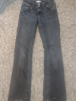 Mörkgrå bootcut jeans - Snygga mörkgrå bootcut jeans med klassisk femficksmodell och kontrastsömmar. Jeansen har en något utsvängd passform nedtill och är tillverkade i ett mjukt denimtyg. Perfekta för en avslappnad och trendig look.