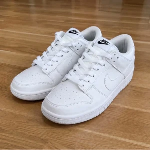 Nike vita låga sneakers - Klassiska vita sneakers från Nike med låg profil och stilren design. Skorna har ovandel i slätt läder, perforerade detaljer på tån och vit sula. Swoosh-logga på sidan och Nike-märke på plösen. Perfekta för en clean och sportig look.