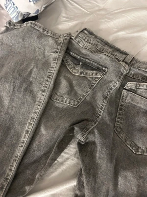 Grå tvättade utsvängda jeans - Säljer ett par grå tvättade jeansfrån gina med utsvängda ben och klassisk femficksmodell. Jeansen har en snygg vintagekänsla och är tillverkade i denim med tydliga sömmar. Perfekta för en avslappnad och trendig look.