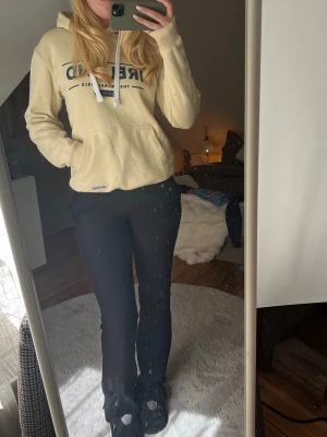 Beige hoodie med tryck och huva - Säljer en beige hoodie med svart tryck framtill där det står 'IRELAND'. Hoodien har en klassisk känguruficka, vita dragsnören och en skön huva. Perfekt för chill dagar och enkel att matcha med jeans eller mjukisbyxor.