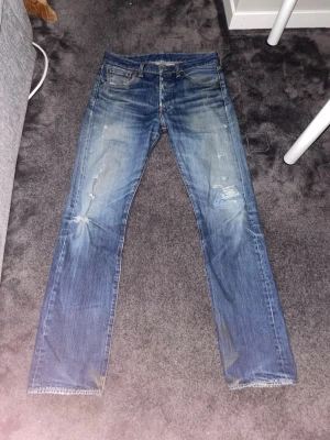 Levis 501 jeans - Säljer ett par unika och eftertraktade vintage 501or i storleken w30 l32. De har feta slitningar och tvättade detaljer men även en snygg lagning. Jeansen har raka ben, klassisk femficksmodell och en cool vintage-look. Perfekta för dig som gillar en avslappnad och trendig stil. Hör av dig vid minsta fundering!😁