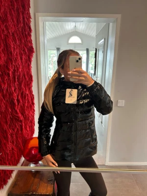  Moncler storlek 1 - Snygg svart dunjacka från Moncler med glansig finish och huva. Jackan har dragkedja framtill och Moncler-logga på ärmen. Perfekt för kalla vinterdagar och ger en trendig look.