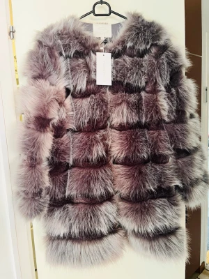 Grå fluffig pälsjacka från Chiquelle - Supersnygg och fluffig pälsjacka i olika nyanser av grått från Chiquelle. Jackan har en boxig passform och stora, mjuka pälspartier som ger en lyxig look. Perfekt för att hålla värmen under kalla dagar och ger en trendig vibe till din outfit.