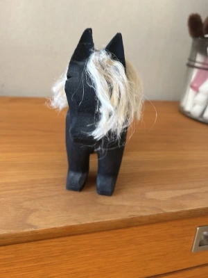 Svart trähäst med ljus man - Dekorativ svart trähäst med ljus, rufsig man i syntetmaterial. Hästen har en stilren och enkel form, perfekt som prydnad på hyllan eller skrivbordet. Passar dig som gillar klassisk svensk design och handgjorda detaljer.