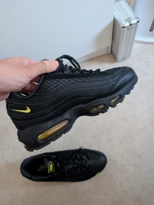 Nike Air max 95 Corteiz - Snygga svarta sneakers med gula detaljer och synlig luftdämpning i sulan. Ovandelen har en mix av slätt och mönstrat material för en cool look. Låg modell med snörning och tydliga street-vibbar. Perfekta för dig som vill sticka ut med stilrena men ändå unika skor. Använts 3 gånger.