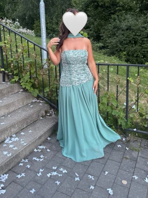 Ljusblå axelbandslös långklänning - Elegant ljusblå långklänning med axelbandslös design och vackert broderat liv i spets. 
