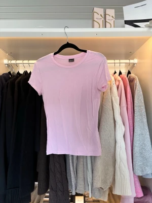 T-shirt  - En basic ljusrosa t-shirt från Gina Tricot i mjuk bomull. Klassisk rund halsringning och korta ärmar. Perfekt att matcha med jeans eller kjol för en enkel och fräsch look.