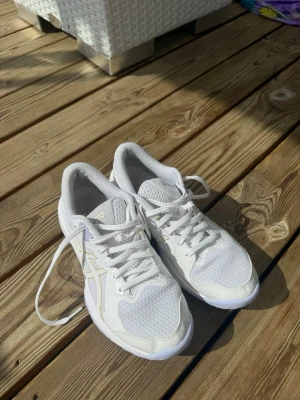 Asics Tränings/Löparskor - Säljer ett par vita sneakers från Asics med mesh- och syntetmaterial. Skorna har klassisk snörning och den ikoniska Asics-loggan i ljusgult på sidan. Perfekta för träning eller vardagsaktiviteter där du vill ha både stil och komfort.
