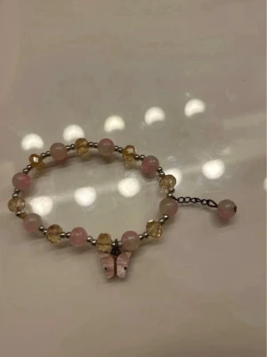 Pärlarmband med fjärilshänge - Sött armband med rosa och gula pärlor samt små silverfärgade detaljer. Armbandet har ett hänge i form av en rosa fjäril som ger en gullig touch. Perfekt accessoar för dig som gillar färg och detaljer. Missfärgad annars fint skick