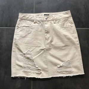 Beige jeans kjol storlek 36 - En beige kjol i mycket fint skick och inte använd många gånger. Kjolen kommer ifrån Nelly och har fin passform. Köparen betalar även frakten.