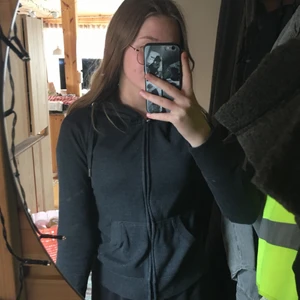 Huvtröja - Grå huvtröja med luva och snören samt fickor bredvid dragkedjan. Knappt använder 