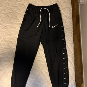 Svarta Nike byxor storlek L  - Sköna Nike nylon byxor köpta från jd sports, med resår längst ner på byxbenen. Samt justerbar midja.