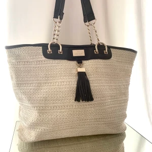 Strandväska från River Island/ fint skick/ beachbag - Rymlig strandväska från River Island i fint skick säljes. Endast använd ett fåtal gånger. Väskan har måtten: H: 35 B: 50 D: 16 cm. Väskan har en rymlig innerficka som stängs med dragkedja. Några lösa trådar inuti väskan, men inget som stör. :)