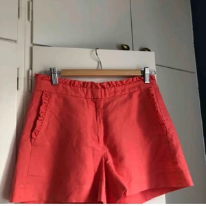 Volangshorts - Korallrosa shorts med volanger i linne & bomull från j.crew. Färgen är mer rosa än orange. Väldigt fina till sommaren. Strl 0, passar XS-S. Fraktkostnad tillkommer. Budgivning från 50kr.