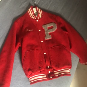 Baseball jacka  - Intressekol på denna Super coola röda baseball jacka från london står inget märke men det är bra material tungt. Det står Aimee och ett stort P på. På bild 2 ser man några små hål på vänstra armen. Annars är den i bra form. Säljer vid bra bud möts upp på Odenplan annars står köpare för frakt 