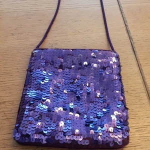 Väska - En fin lila paljettväska lite sliten har användes en del är ett par år gammal är väldigt liten vet inte om man får plats med en telefon men i alla fall en plånbok.