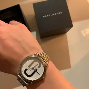 Marc Jacobs klocka som är använd endast ett fåtal gånger. Analogstid visas med tre visare, streck, punkter och bokstäver. Klockan 36cm bred och har ett reptåligt mineralglas. Frakten är inräknad i priset 