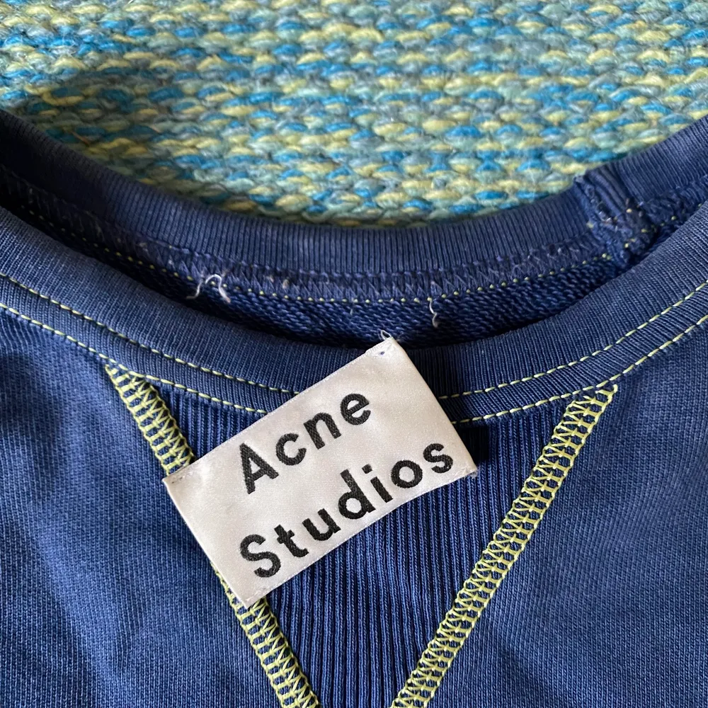 Säljer en blå tröja sweatshirt från Acne Studios med gröna detaljer. Tröjan är använd fåtal gånger och har inga som helst defekter eller liknande, förutom att taggen i nacken trillat av av sig självt (se bild 3) men den går lätt att sy på igen om man skulle vilja det. Storleken är XS men skulle säga att den sitter som en S. . Tröjor & Koftor.