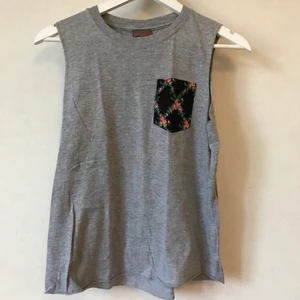 Grått linne med ficka, XS-S - Så fint linne eller t-shirt i grått med en liten ficka med blommor på. Finfint skick! 100% bomull.  Kan mötas i Stockholm eller skicka mot fraktkostnad! ✨🌸✨