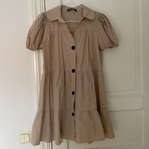 Klänning  - Säljer en utläcker beige klänning i stlr S. helt slutsåld. Använd 2 gånger, och är i gott skick. Snygga detaljer som puffärmar och svarta knappt. Skriv vid intresse. Frakt står du för🤍