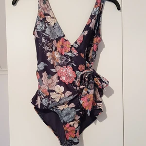 Blommig V-ringad baddräkt 🌸 - 🌸Baddräkten är använd en gång och är i nyskick.      🌸Baddräkten är sydd i omlott och har en knytning på vänster sida