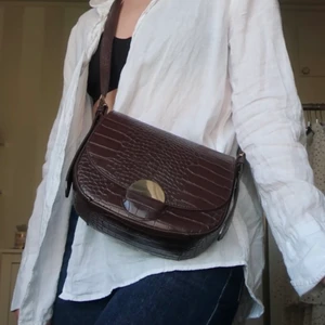 Handväska    - Supersnygg brun väska i läderimitation. Guldigt knäppe med magnet. Kan verkligen fullända en outfit 😍 Lite repor på knäppet men annars i jättefint skick. Köparen står för frakten. 