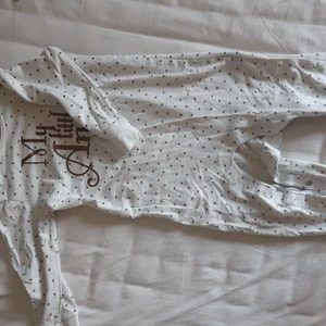 Vit pyjamas med stjärnor, vingar samt text från Baby Lindex - Använt ett par gånger men är i bra skick. Har små guldstjärnor över hela sig, tryck på baksidan som är vingar samt ett tryck på framsidan som är en text där det står "My Little Angel". Alla trycken är i bra kvalité.