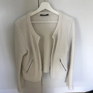 Kofta - Vit kofta med detalj av dragkedja längst ner på ärmarna. 