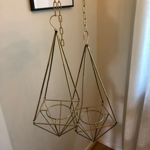 Amplar i guld  - Två amplar i guld med kedja. Amplarna är ca 40 cm höga och i dem får det plats krukor som är ca 8 cm breda.