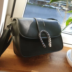 Handväska med axelband. - Mörk mossgrön väska med en snygg metallic detalj. Väskan är i nytt skick då den bara legat i garderoben. 