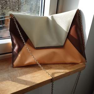 Kuvertväska som också går att använda som vanlig handväska med kedje axelrem. Färgerna är brun vit och aprikos. Kedjan är guldfärgad. 