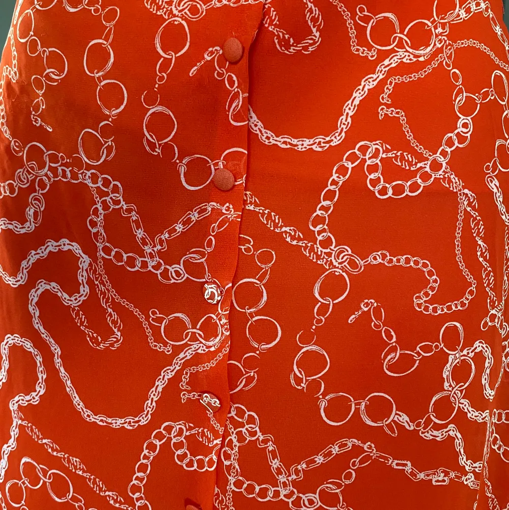 En kjol köpt från en butik på Turkiets flygplats. Väldigt fin och väldigt bekväm. Endast använt 2 gånger under semestern, växte ur den snabbt. Det är ett mesh material på utsidan med snyggt mönster, undertill finns det en underkjol. Midjebandet är inte justerbart, på sidan sitter en dragkedja. Den är en orange/röd färg, med vitt mönster.. Kjolar.