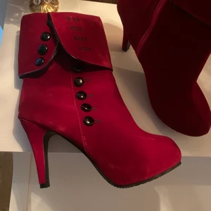 Snygga högklackade skor i mocka - Helt nya högklackade skor i mocka. Vinröda med snygga knappdetaljer. Dragkedja på insidan. Storlek 40. Klackhöjd 10cm. 