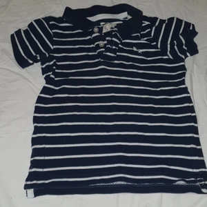 T-shirt barn strl 86 - Pikétröja till barn, storlek 86. Mörkblå/vit.  Rensar på vinden, kommer lägga ut en hel del grejer. Kan skickas, då du betalar frakten.