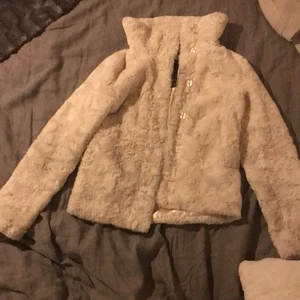 En vit pälsig jacka med knappar  - Den har knappar och är päls