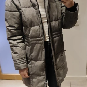Lång skön vinterjacka/kappa strl Small - skön vinterjacka från Take Off i storlek Small. Syntetdun (polyester) sköna muddar i armslut, avtagbar huva. Innerficka och sidofickor på bägge sidor, alla med dragkedja. Använd men hittar inget att anmärka på. Nytvättad och ser i princip ny ut. Nypris var 999kr. Säljes för 300kr + frakt 99kr