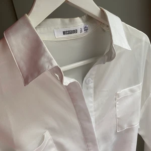 Längre skjorta i glansigt material - Vit skjorta i längre modell från Missguided. Glansigt material och band i midjan. Storlek 34 men passar även 36. Endast använd 2ggr. 
