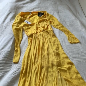 Gul klänning - Aldrig använd, kommer med prislapp.  Från Nelly.com. Den är gul och är v ringad med en slit där nere. Säljer pågrund av att jag aldrig använt för att den inte är riktigt min stil. Orginalpris 498kr men säljer den för 100kr + frakt.
