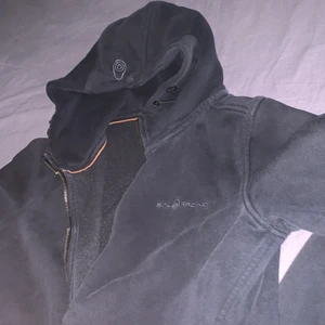 Snygg hoodie! - Snygg sail racing hoodie. Den är svar men var svårt att få det svara att se svart ut på bild!!! Den är i fint skick utöver att det man dra i för att dra igen dragkedjan är sönder, men det har ej varit ett problem för mig. Sail märket finns på ena bröstsidan och på luvan.